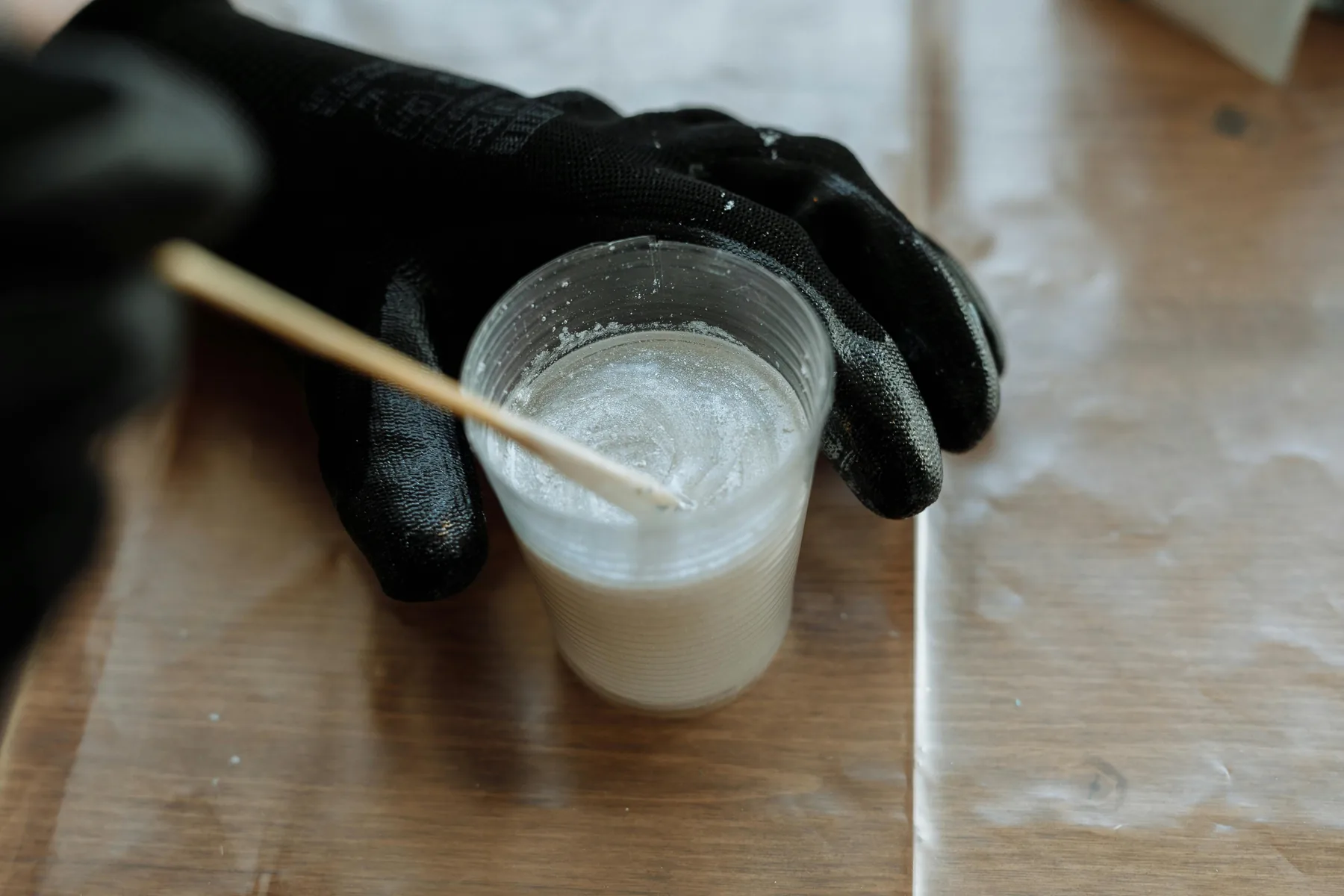 Gloved hand mixing two-part coating resin in a cup on a work surface